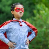 A young child wearing a red superhero cape and mask stands confidently outdoors, symbolizing the empowering impact of ninja warrior training for kids.