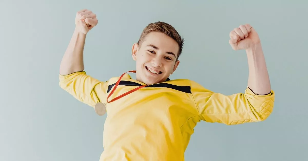 A smiling boy wearing a medal and celebrating his success, representing the self-esteem kids gain through ninja warrior training for kids.