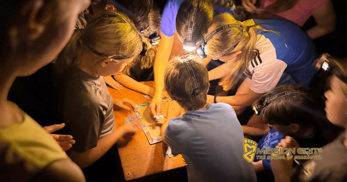 Children wearing headlamps working together on a hands-on team challenge indoors at a confidence-building summer camp.