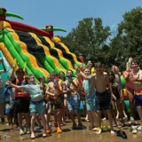 Children playing with water blasters in front of a large inflatable water slide at one of Mission Grit's summer camps for shy kids Charlotte NC location.