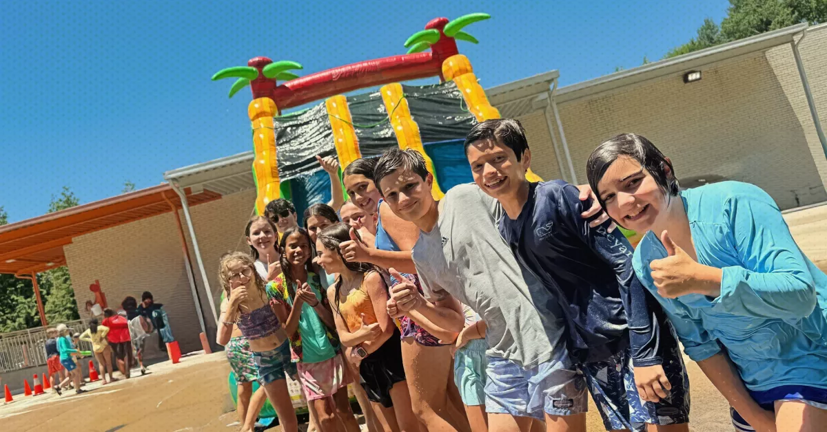 Group of kids smiling and giving thumbs up in front of an inflatable slide at a noncompetitive summer camp in Charlotte.