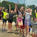 Kids jumping and cheering outdoors during an active spring break camp in Charlotte.