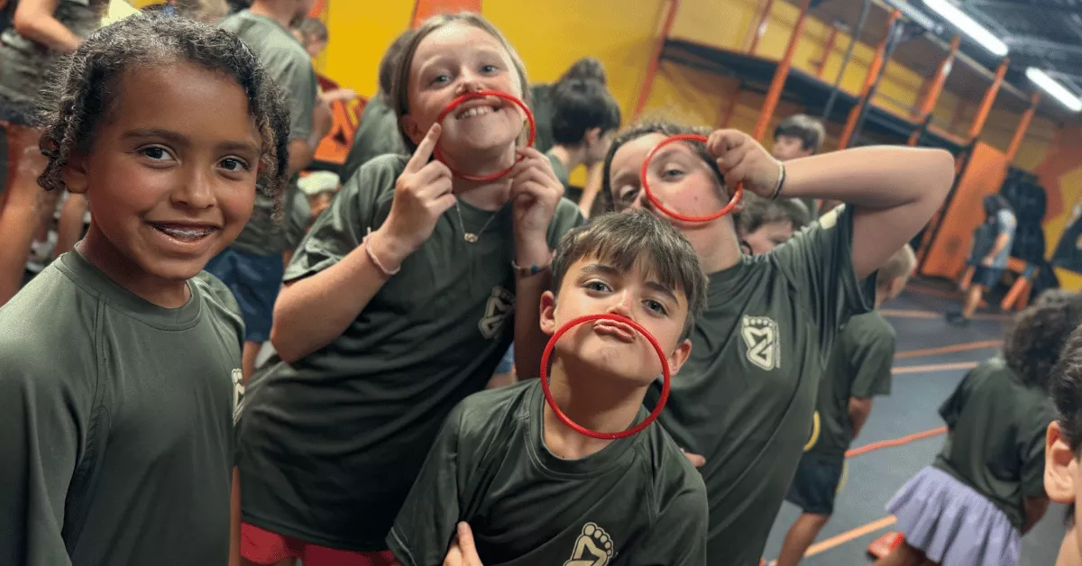 Smiling kids posing with red rings during an indoor camp activity, representing what to pack for teacher workday camp.