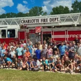 Large group of campers at their first summer camp Charlotte NC pose outdoors in front of a Charlotte Fire Department rescue truck.