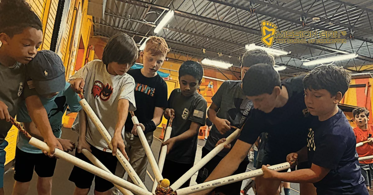 A group of boys works together indoors using PVC pipes to guide a small ball in a hands-on teamwork activity.