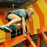 Girl balances mid-movement on an indoor obstacle course with bright orange structures and yellow striped walls at Mission Grit Xplor program Charlotte.