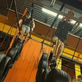 Children make their way across hanging tires and rope obstacles inside a brightly colored Mission Grit indoor gym.