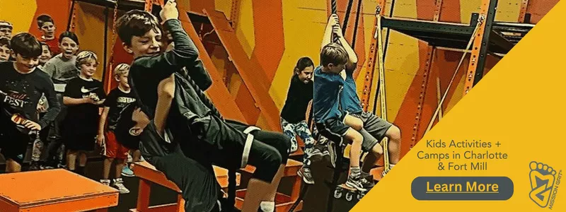 Children at an indoor obstacle gym swing on ropes while other kids wait nearby, beside a yellow panel promoting kids activities and camps in Charlotte and Fort Mill with a “Learn More” button.