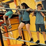 Children carefully cross a metal balance obstacle inside a brightly colored indoor training gym, at Mission Grit obstacle course birthday party Charlotte & Fort Mill.