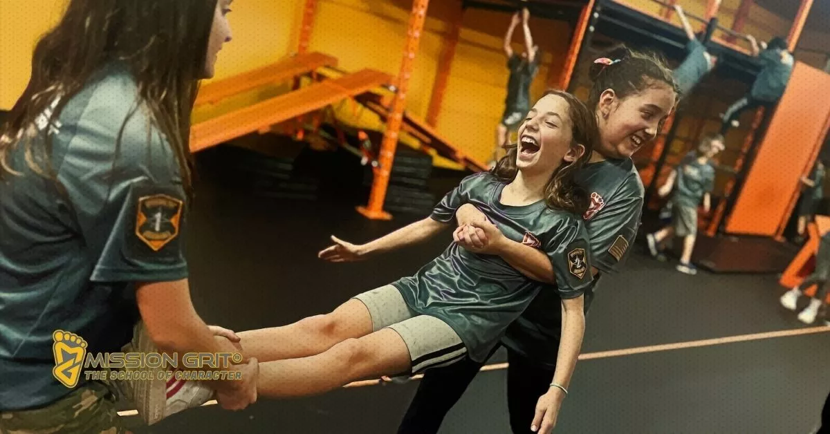 Girls laugh during a partner-based teamwork activity inside Mission Grit’s indoor training space.