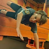 Child crawling across an indoor obstacle during a Mission Grit kids fitness activity.