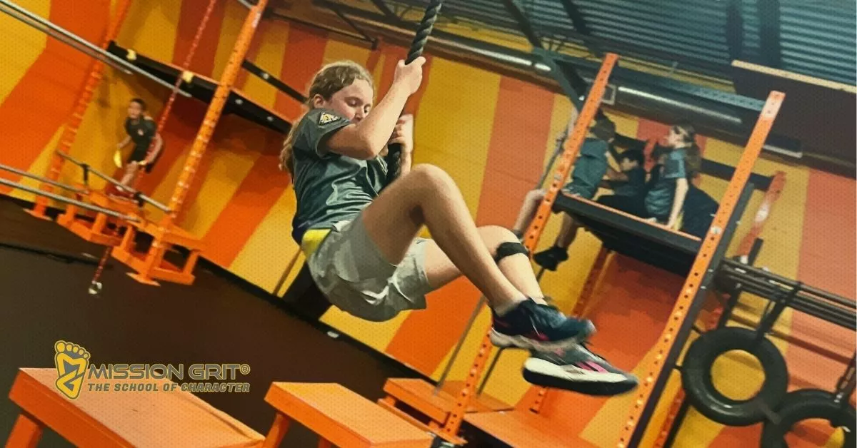 Child swinging on a rope during an indoor Mission Grit obstacle course challenge.